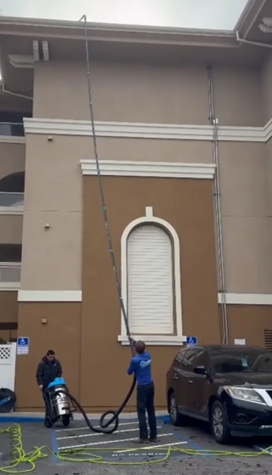 Crew vacuuming a third-story gutter on a commercial building from the parking lot